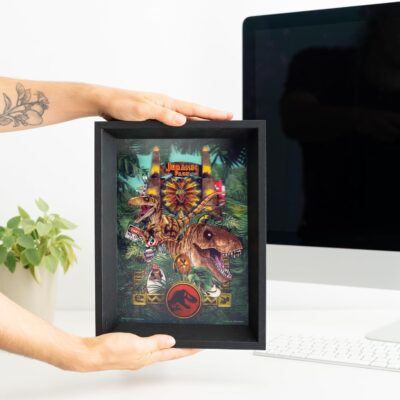 Framed artwork of a dinosaur with 'Jurassic Park' logo held by a person.