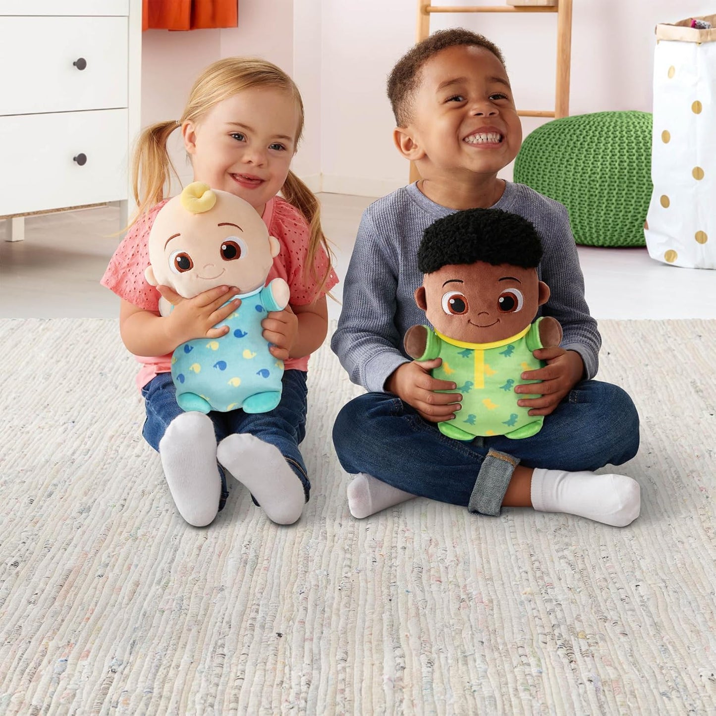 Two children sitting on the floor holding baby dolls in a room with a white carpet.